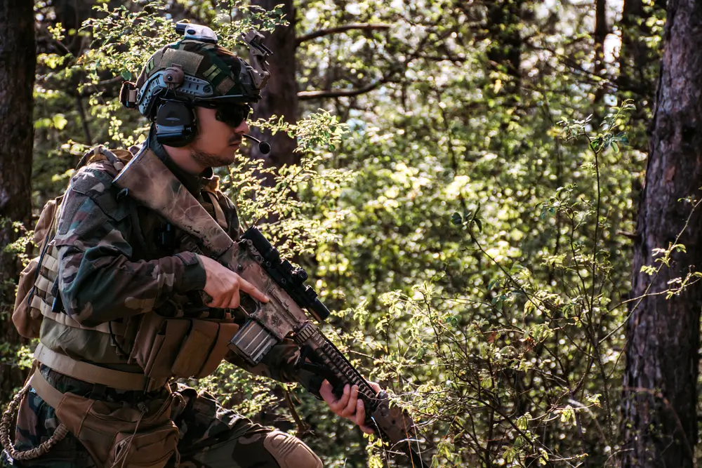 Soldat en forêt équipé d'un casque balistique, d'un gilet pare-balles tactique et d'un fusil de combat.