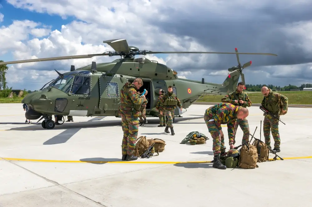Soldats belges préparant leurs sacs à dos militaires sur le tarmac devant un hélicoptère.
