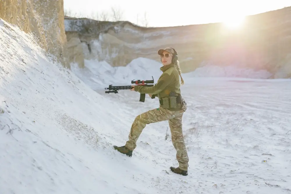 Militaire en tenue tactique s'exerçant au maniement d'armes lors d'un entraînement sur un terrain sablonneux.