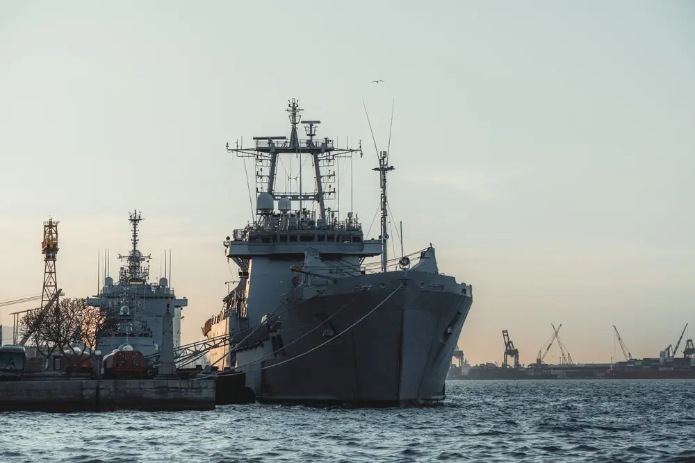Navire militaire de la Marine belge amarré dans une base navale avec des grues portuaires en arrière-plan.