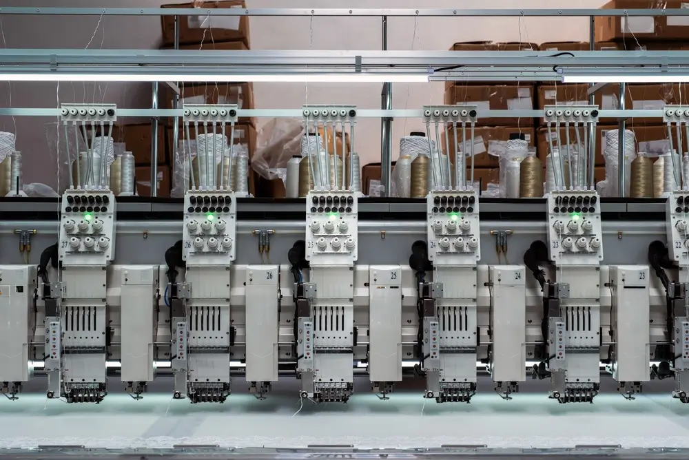 Machines à broder industrielles alignées dans une usine textile pour la fabrication d'uniformes militaires.