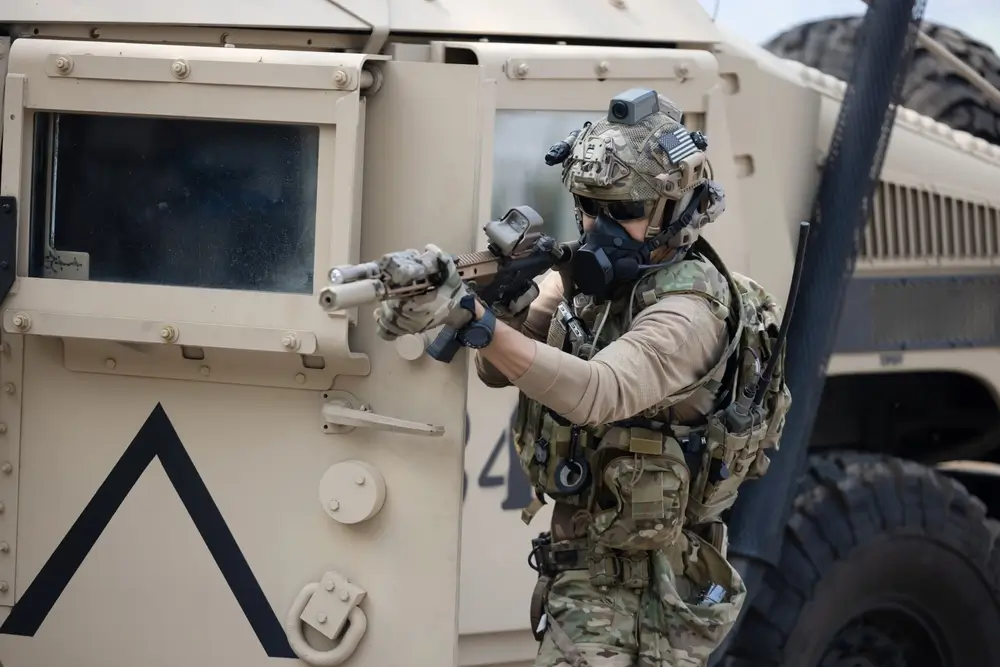 Belgische soldaat in opleiding die met zijn geweer richt vanuit de dekking van de deur van een militair pantservoertuig Griffon.
