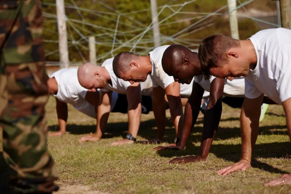 Militaire rekruten in wit T-shirt die pompoefeningen uitvoeren op het gras tijdens een fysieke training.