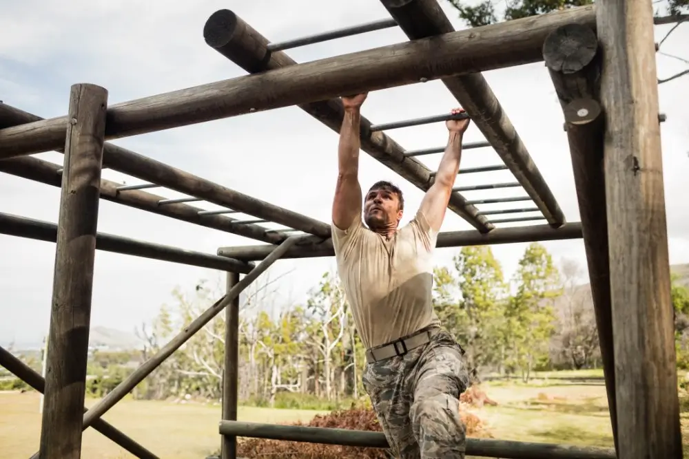 Candidat militaire franchissant des barres en bois sur un terrain d'entraînement extérieur durant sa formation.