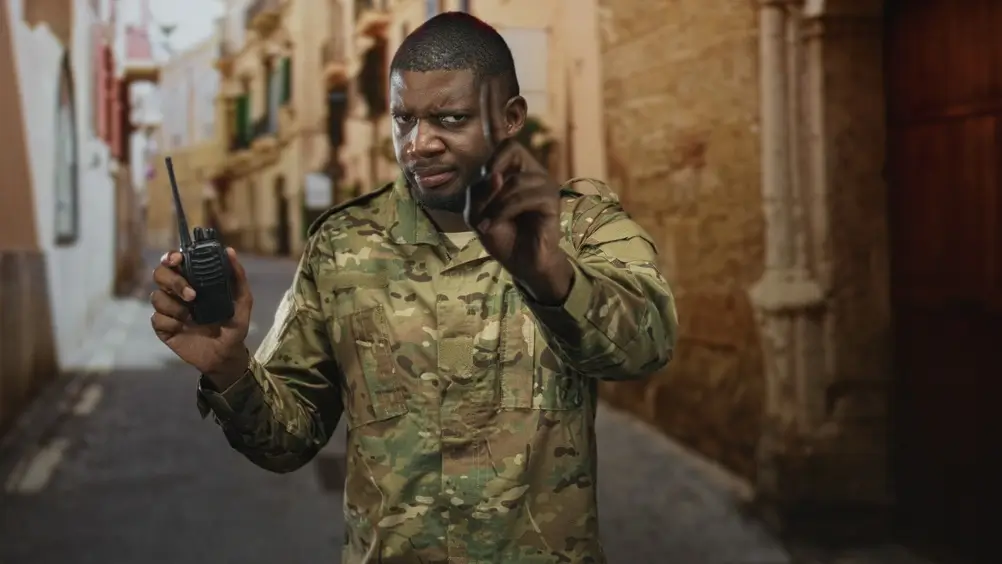 Jonge militair in camouflage-uniform tijdens een stadspatrouille, die een walkietalkie vasthoudt tijdens een missie.
