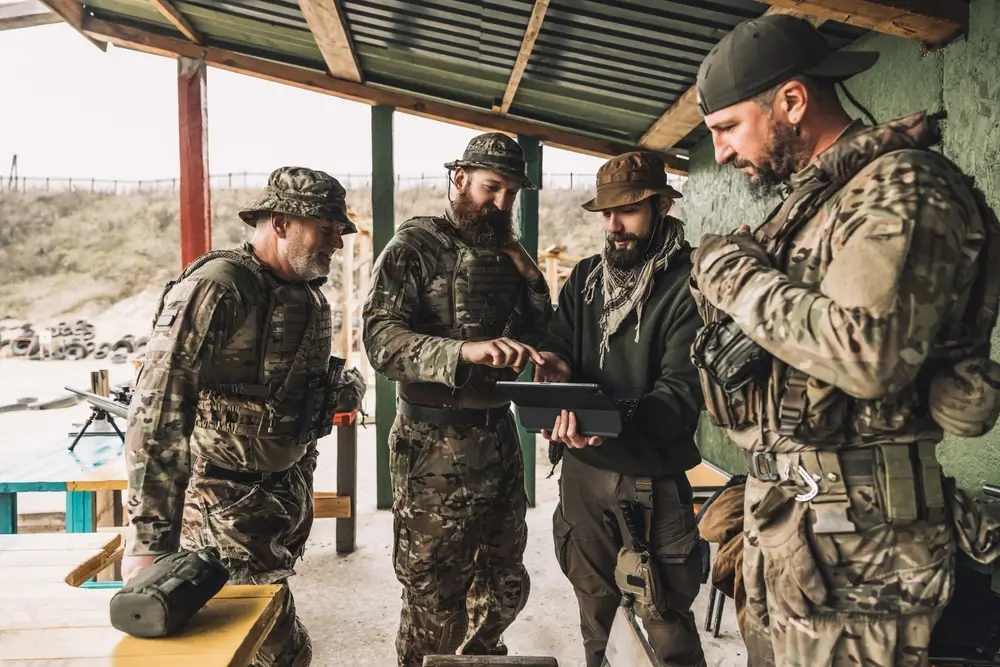 Militaires en tenue tactique collaborant autour d'une tablette lors d'un briefing, illustrant le travail d'équipe.