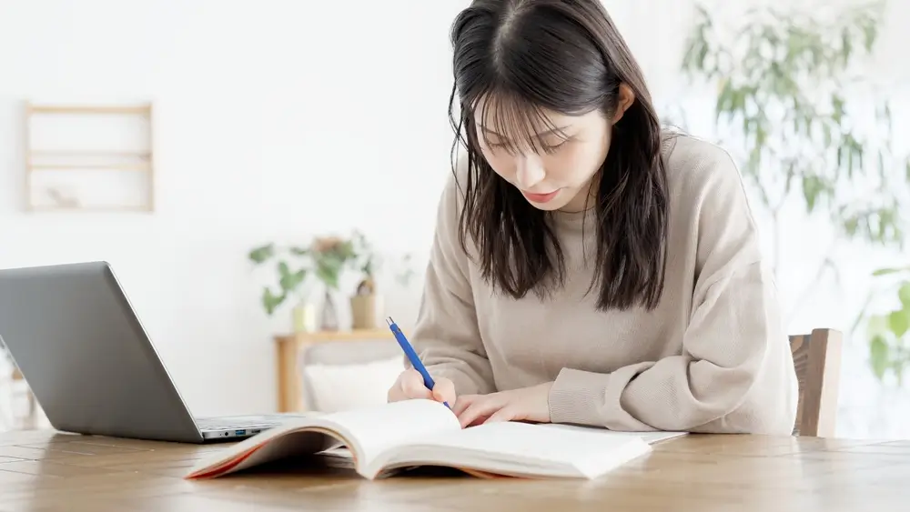 Une étudiante étudie seule avec un cahier d'exercices et son ordinateur pour se préparer aux tests de la Défense.