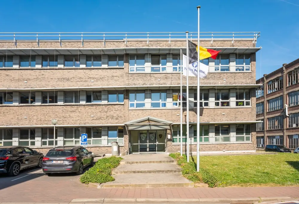 Bâtiment administratif d'une caserne militaire belge avec drapeaux et parking, lieu de formation pour les réservistes.