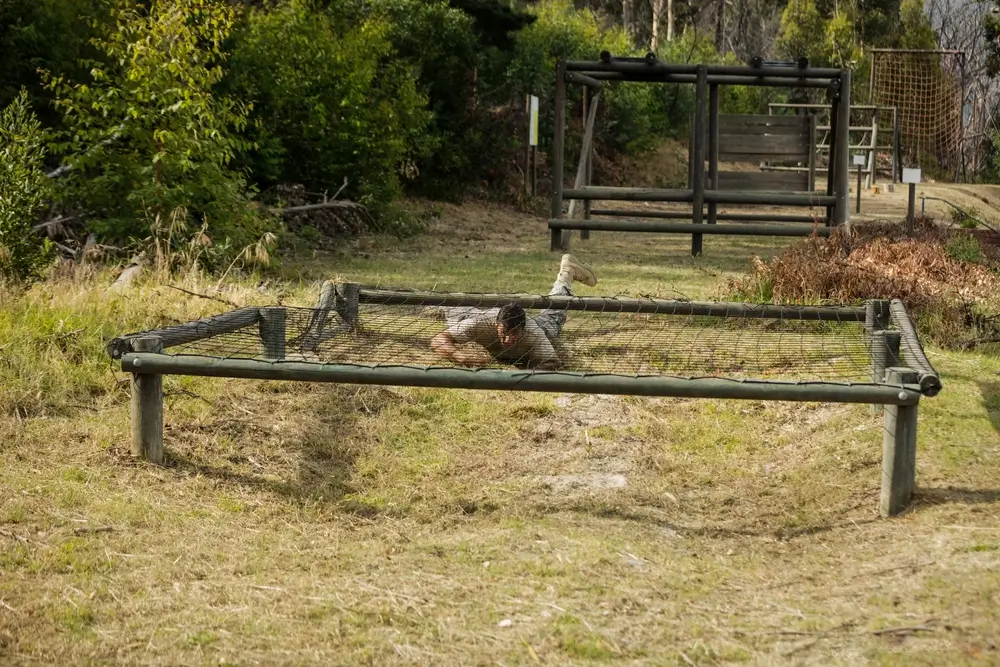 Un soldat rampe sous un filet lors d'un parcours d'obstacles pendant sa formation militaire.