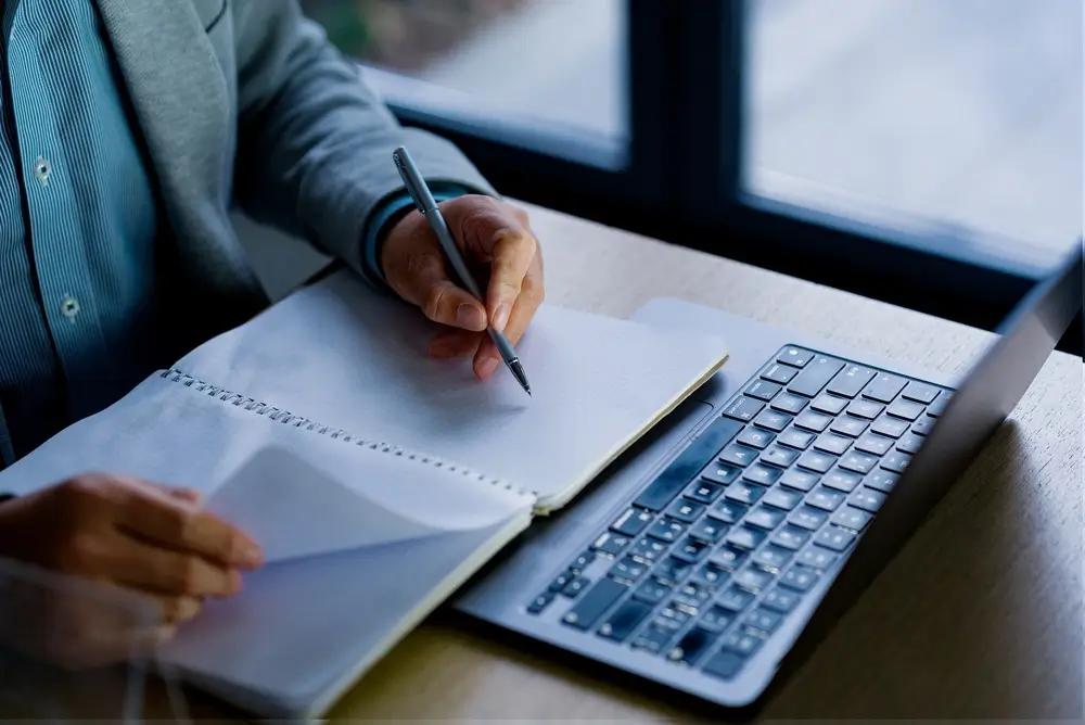 Candidat prenant des notes devant son ordinateur portable lors d'un test informatique de recrutement.