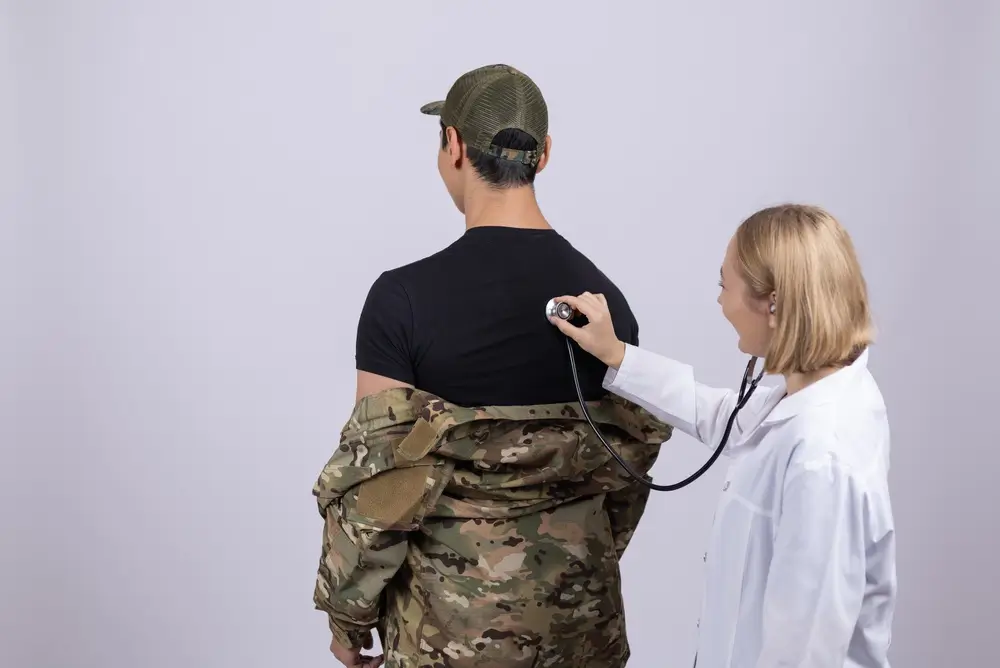 Médecin militaire auscultant un candidat en uniforme lors d'un examen d'aptitude médicale.