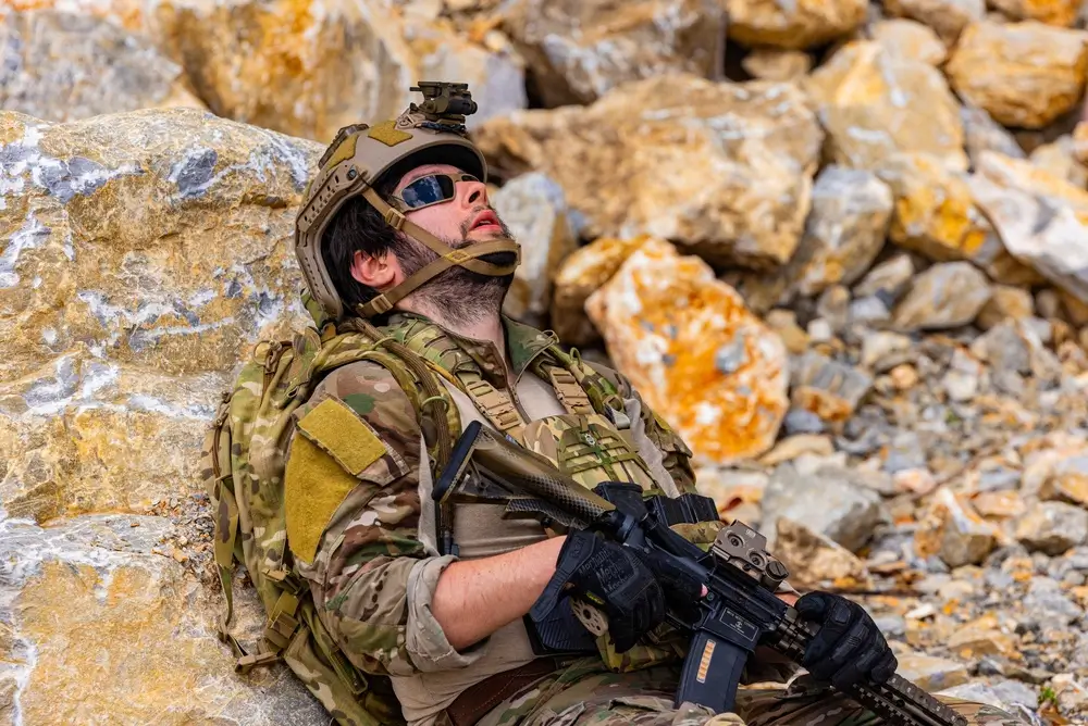 Une recrue militaire épuisée s'appuie contre des rochers lors d'un entraînement physique intensif sur le terrain.