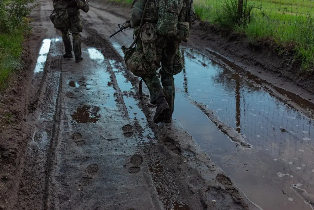 Soldats réservistes marchant sur un chemin boueux avec leur équipement lors d'un entraînement militaire.
