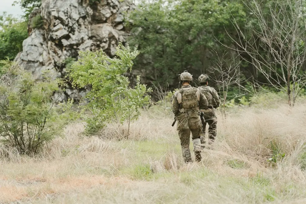 Deux soldats belges en tenue de camouflage effectuent une patrouille en forêt au sein d'une unité militaire.