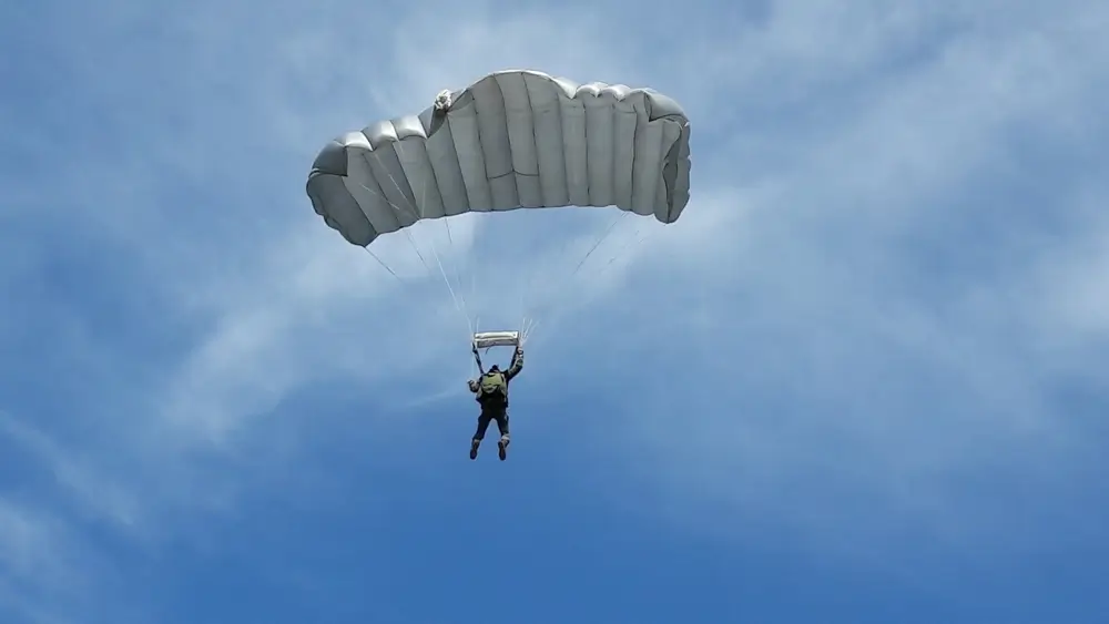 Un parachutiste descend dans un ciel bleu avec son parachute déployé lors d'un exercice de saut para-commando.