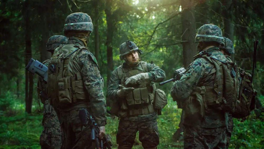 Sous-officier chef d'équipe de l'armée belge donnant des instructions tactiques à ses soldats lors d'un exercice en forêt.